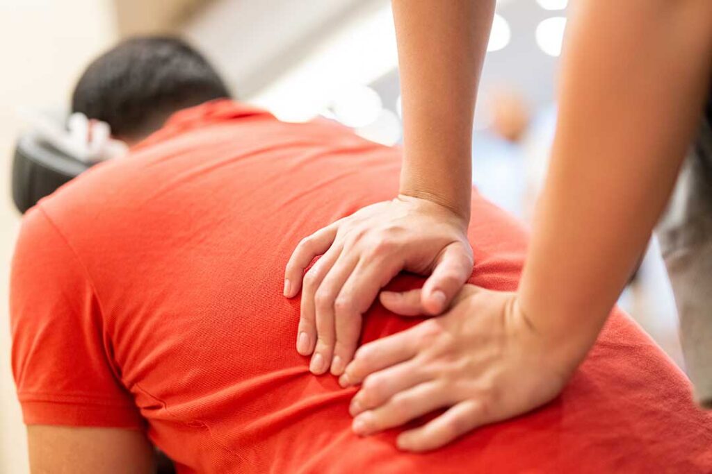 A healthcare provider demonstrates a gentle spinal adjustment to an adult patient in a bright clinic room.